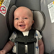 Deklan is registered to the contest to win money with this photo: baby, smiling, car_seat, infant, child, happy, safety_harness, clothing, cute, seat, head_support, person, indoors, young_child, face, joy, comfort, secure, blue_pants, onesie