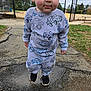 autumn_leaves, blue_eyes, car_prints, chainlink_fence, child, curious_expression, face, grass, gray_sweatshirt, outdoor, pavement, playground, portrait, puddle, rosy_cheeks, sneakers, sports_field, standing, toddler, trees