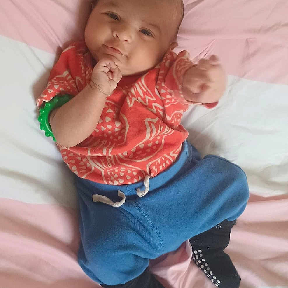 Aarush joined the competition — help win amazing prizes! baby, bed, black_socks, blue_pants, bracelet, child, clothing, cute, expression, face, hand, indoors, infant, lying_down, person, portrait, red_shirt, smiling, soft_light, young