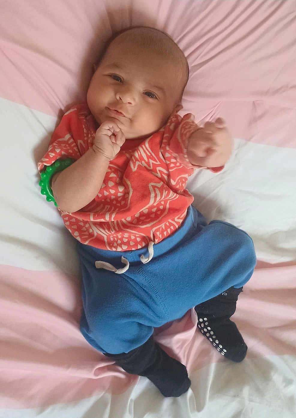 Aarush joined the competition — help win amazing prizes! baby, infant, child, cute, lying_down, bed, clothing, red_shirt, blue_pants, black_socks, bracelet, smiling, face, person, indoors, soft_light, portrait, hand, expression, young