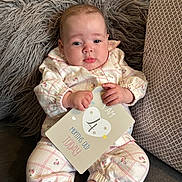 Nellè is registered to the contest to win money with this photo: baby, infant, milestone_card, clothing, pillow, fluffy, cute, face, hand, foot, sitting, patterned_clothes, pink, white, indoor, portrait, child, young_baby, couch, soft_texture