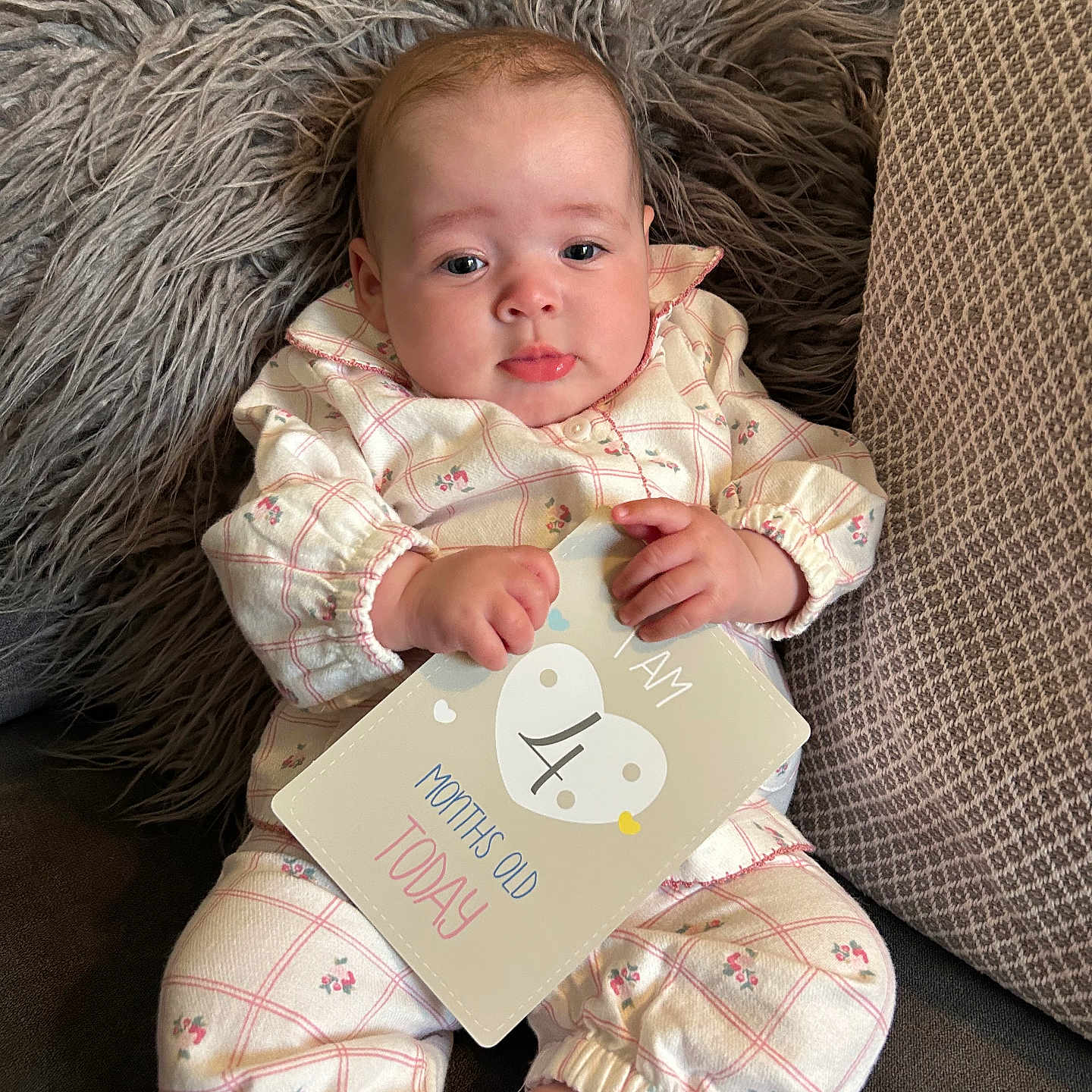 Nellè is registered to the contest to win money with this photo: baby, child, clothing, couch, cute, face, fluffy, foot, hand, indoor, infant, milestone_card, patterned_clothes, pillow, pink, portrait, sitting, soft_texture, white, young_baby