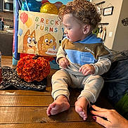 Breckin is registered to the contest to win money with this photo: toddler, child, birthday, gift_bag, balloons, cartoon, pumpkin, curly_hair, table, barefoot, sitting, indoor, clothing, hand, nail_polish, kitchen, decor, celebration, person, portrait
