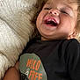 Breckin is registered to the contest to win money with this photo: toddler, child, smiling, laughing, black_shirt, text_on_shirt, wild_and_free, curly_hair, blanket, cozy, close_up, happy, face, person, casual_clothing, indoor, soft_texture, cute, joyful, portrait