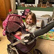 Aryanna participe au concours pour gagner de l'argent avec cette photo : child, toy_stroller, doll, indoor, wooden_floor, furniture, curtains, smiling, young_child, playtime, pink, purple, window, home, person, casual_clothing, flooring, toy, happy, room