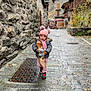 Aryanna participe au concours pour gagner de l'argent avec cette photo : toddler, child, winter_clothing, pink_hat, scarf, mittens, baguette, cobblestone_street, stone_wall, old_buildings, outdoor, walking, cute, cold_weather, footwear, urban, daytime, person, small_child, travel