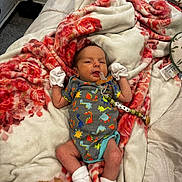 Arlo is registered to the contest to win money with this photo: baby, infant, blanket, floral_pattern, onesie, dinosaur_print, mittens, socks, pacifier, clip, bed, soft, cozy, indoor, person, newborn, cute, resting, comfort, sleepwear