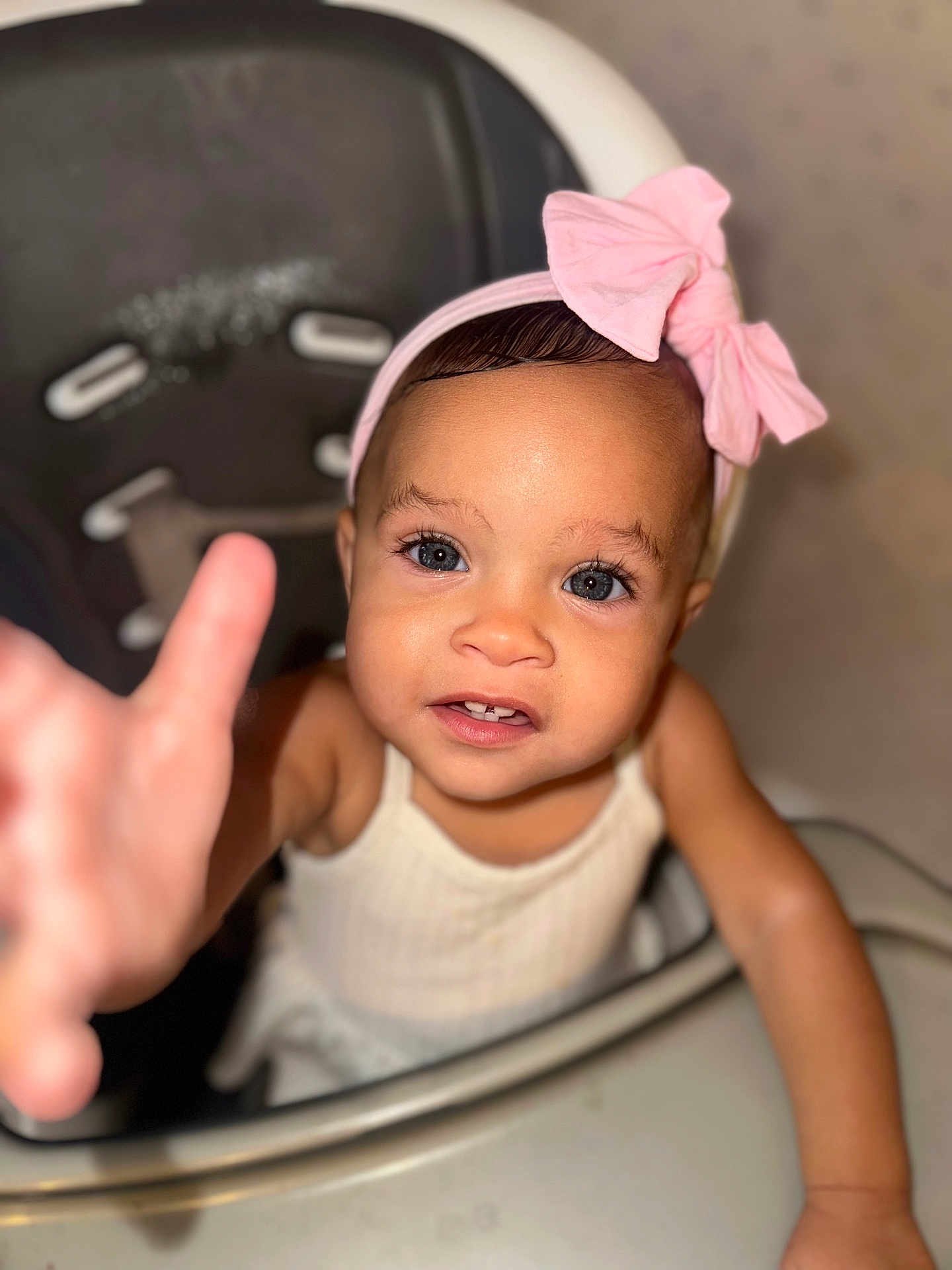 Serenity is registered to the contest to win money with this photo: toddler, child, baby, high_chair, pink_bow, headband, reaching_hand, curious, portrait, indoor, face, eyes, skin, clothing, expression, person, furniture, seat, closeup, cute