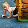 Penelope is registered to the contest to win money with this photo: toddler, child, crawling, playground, blue_carpet, pink_shirt, black_shorts, indoor_play_area, curly_hair, pigtails, smiling, play_structure, colorful, fun, cute, young_child, exploring, happy, small_hands, kneeling