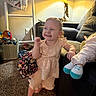Penelope is registered to the contest to win money with this photo: toddler, child, smiling, indoor, carpet, dress, barefoot, toy, doll, lamp, furniture, living_room, basket, blanket, curtain, happy, person, cute, couch, home