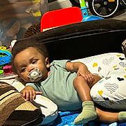 Donta is registered to the contest to win money with this photo: toddler, pacifier, blanket, cushion, child, toy, tricycle, sock, indoor, relaxed, baby, clothing, floor, playroom, comfort, home, colorful, furniture, person, resting