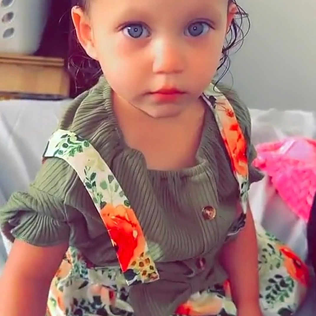 Novaleigh joined the competition — help win amazing prizes! toddler, child, baby, blue_eyes, sitting, dress, floral_pattern, green_top, indoor, bed, laundry_basket, hair, face, expression, skin, clothing, person, cute, portrait, text_overlay