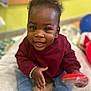 Ilétou a rejoint le concours — aidez-le/la à gagner de superbes lots ! baby, child, smiling, happy, indoor, toy, clothing, maroon_sweater, jeans, black_shoes, curly_hair, face, person, infant, cute, playful, sitting, bright, colorful, young