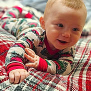 Declan joined the competition — help win amazing prizes! baby, child, pajamas, smiling, face, hand, blanket, plaid, pattern, bedroom, indoor, cute, infant, happy, person, young, cozy, clothing, holiday, red