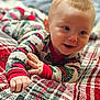 baby, child, pajamas, smiling, face, hand, blanket, plaid, pattern, bedroom, indoor, cute, infant, happy, person, young, cozy, clothing, holiday, red