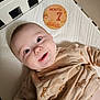 baby, crib, infant, smiling, face, clothing, onesie, wooden_sign, month_marker, happy, child, bed, white, pattern, horse, cute, portrait, young, indoors, sleeping_area