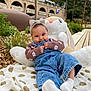 Maya a rejoint le concours — aidez-le/la à gagner de superbes lots ! baby, child, infant, cute, denim_overalls, headband, bow, plush_toy, bunny, blanket, outdoor, greenery, plants, wood_chips, smiling, sock, candid, playful, portrait, person
