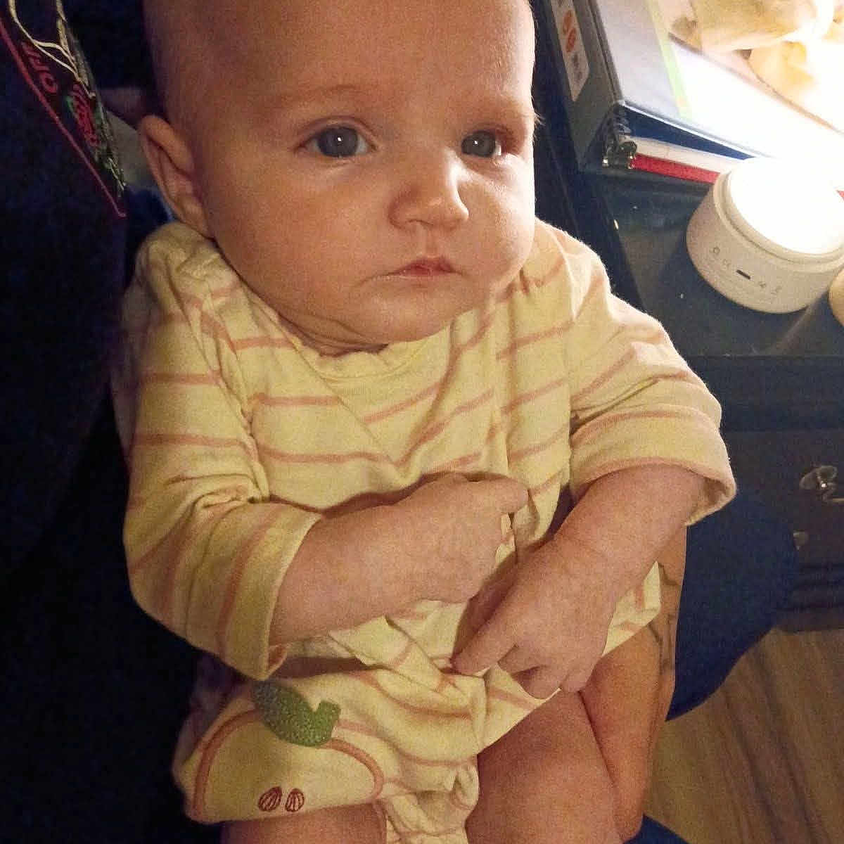 Lakota joined the competition — help win amazing prizes! baby, infant, child, person, yellow_clothing, striped_clothing, indoor, holding, face, hands, legs, binder, table, device, furniture, curious, portrait, candid, human, seated