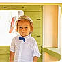 toddler, child, hat, bucket_hat, bow_tie, white_shirt, playhouse, green_wall, curious, portrait, indoor, young_child, casual_clothing, face, expression, person, standing, cute, fashion, light