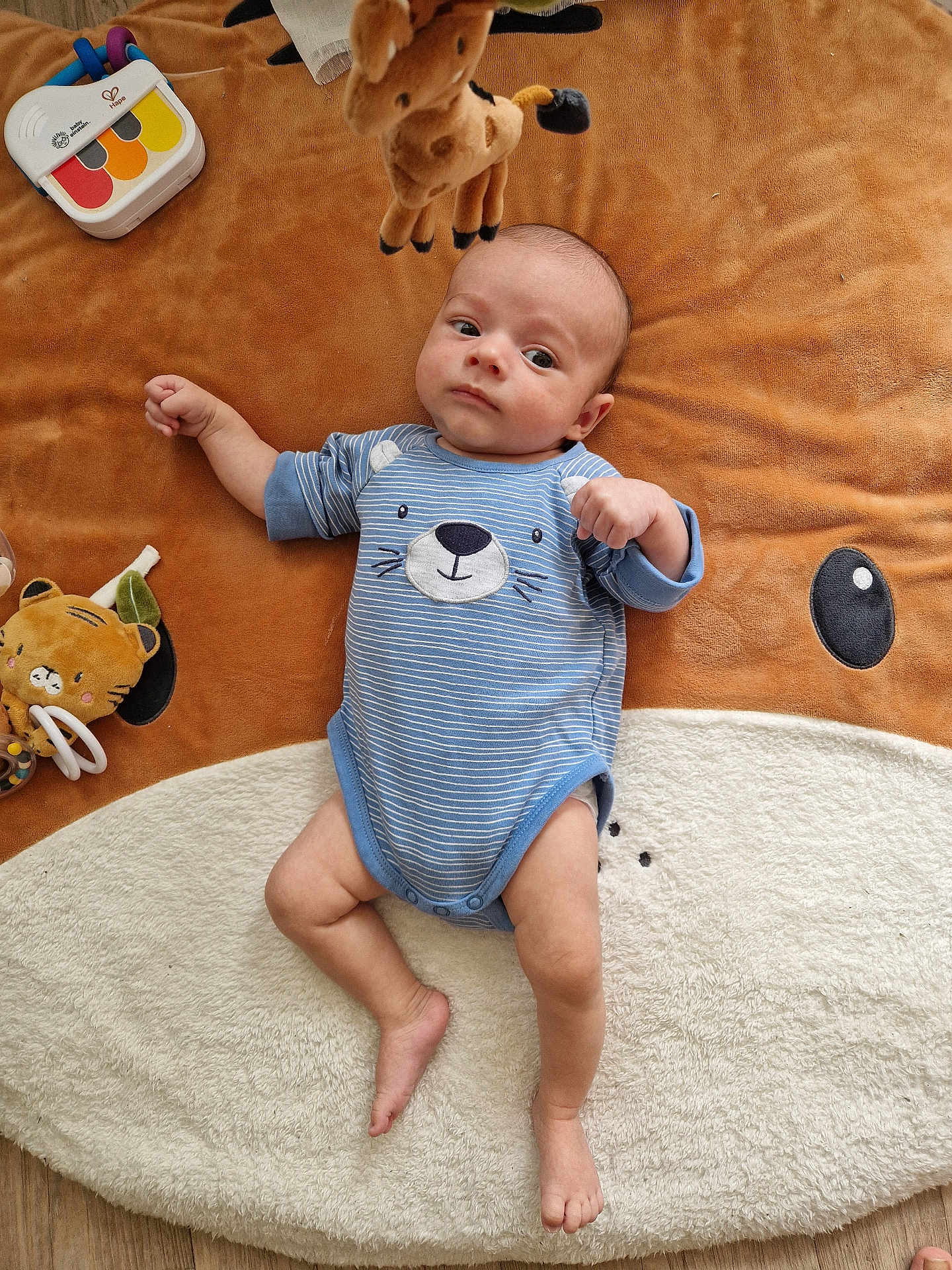 Arthur a rejoint le concours — aidez-le/la à gagner de superbes lots ! baby, infant, blue_onesie, plush_toy, giraffe_toy, animal_blanket, floor, wooden_floor, baby_piano, child, cute, lying_down, soft_texture, indoors, playtime, toy, small_foot, face, expression, comfortable