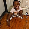 child, toddler, smiling, indoor, wooden_floor, door, white_door, squatting, happy, person, floor, casual, clothing, shorts, tshirt, black_hair, curly_hair, technology_interface, snapchat, mobile_screen