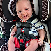 Benjamin is registered to the contest to win money with this photo: baby, car_seat, graco, smiling, happy, child, infant, seatbelt, clothing, red_shorts, striped_shirt, face, head, legs, feet, hand, safety, child_seat, portrait, indoor