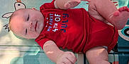 Benjamin joined the competition — help win amazing prizes! baby, infant, child, red_onesie, play_mat, hand, foot, skin, face, smile, light_shadow, text_on_clothing, celebration, holiday, cute, indoors, person, lying_down, young, toddler