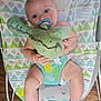 baby, blue_eyes, bouncer, child, chubby_legs, colorful, comfort, crocodile, cute, holding, indoor, infant, knitted_toy, pacifier, patterned_fabric, playful, seated, smiling, toy, wooden_floor