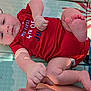 baby, infant, red_onesie, celebration, holiday, 4th_of_july, patriotic, child, cute, skin, foot, hand, finger, mat, pattern, playful, outdoor, sunlight, person, lying_down