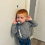 toddler, child, indoor, pacifier, red_hair, jeans, gray_shirt, standing, wooden_floor, door, wall, curious, person, casual_clothing, young_child, baby, clothing, floor, leaning, pacifier_clip