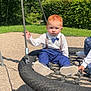 child, toddler, swing, playground, outdoor, rope_swing, grass, trees, sunlight, shadow, red_hair, blue_pants, white_shirt, bow_tie, suspenders, shoes, hand, person, gravel, nature