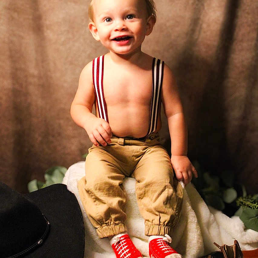 Elias is registered to the contest to win money with this photo: accessories, baby, boot, clothing, costume, face, footwear, hat, head, jeans, pants, person, photography, portrait, sandal, shoe, shorts, sitting, sneaker, suspenders