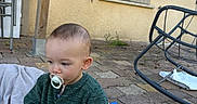 Julian participe au concours pour gagner de l'argent avec cette photo : toddler, child, pacifier, building_blocks, outdoor, blanket, pavement, window_shutter, wooden_post, garden_furniture, curious, sitting, clothing, shorts, sweater, toy, playtime, daylight, casual, backyard