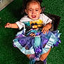 toddler, crying, child, birthday, tutu, colorful_clothing, artificial_grass, sitting, upset, cushion, portrait, hair_buns, earrings, footwear, indoor, celebration, expression, person, young_child, emotional