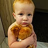 child, baby, toddler, red_hair, blue_eyes, stuffed_animal, plush_toy, indoor, earrings, diaper, floor_tiles, wooden_door, expression, cute, portrait, hugging, person, young_child, skin, curly_hair