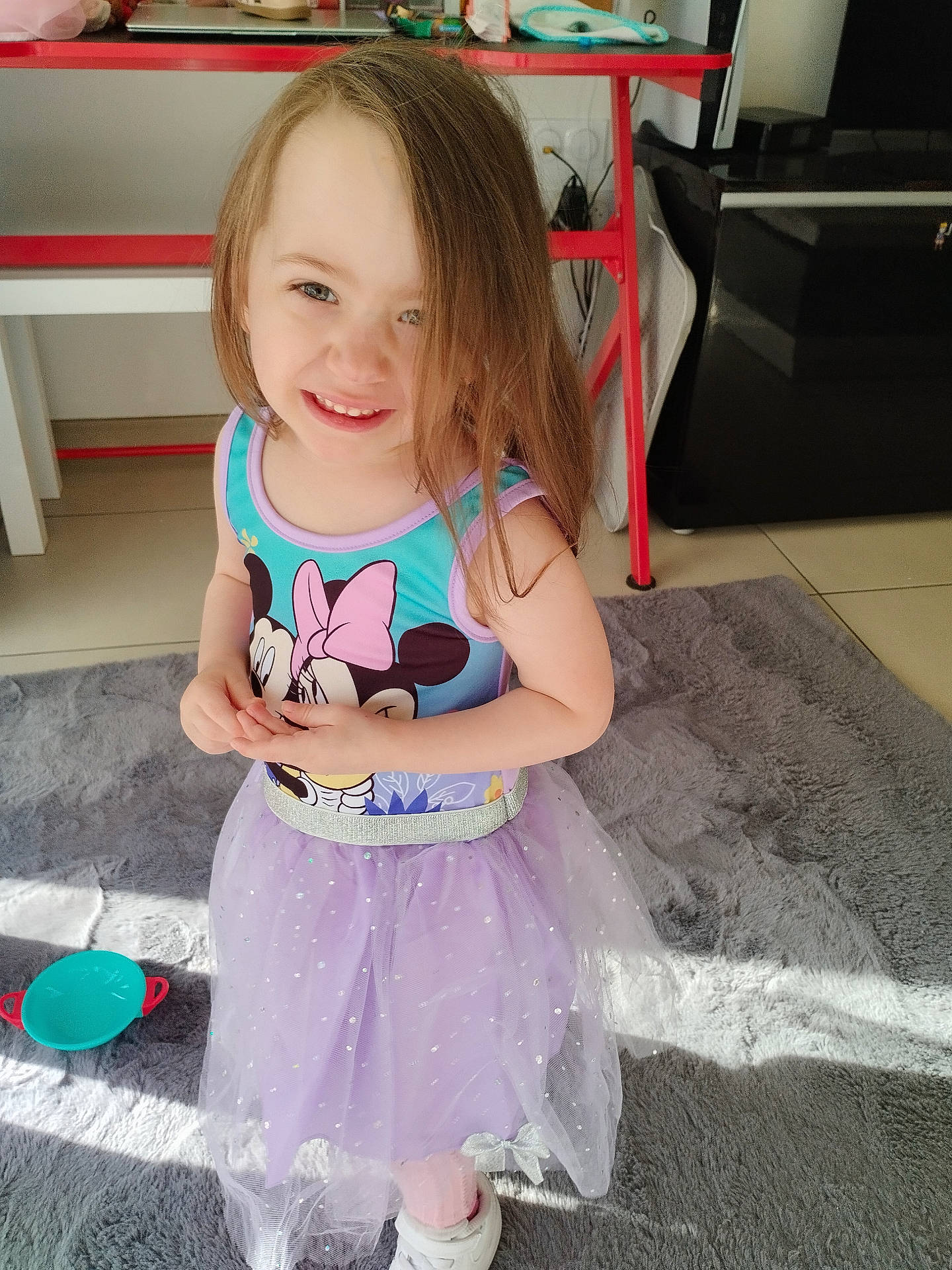 appliance, child, clothing, dress, floor, footwear, girl, hair, happy, indoor, kitchen, person, playful, rug, smiling, sunlight, table, tank_top, toy, tutu
