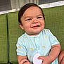 baby, child, smiling, onesie, banana_pattern, green_couch, brush, hand, indoor, cute, happy, infant, person, holding, seated, short_hair, skin, face, arm, furniture