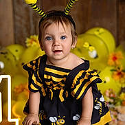 Ainhoa is registered to the contest to win money with this photo: child, toddler, baby, bee_costume, headband, antennae, blue_eyes, smile, portrait, studio_photo, yellow_balloons, wooden_background, barrel, party_decoration, flowers, striped_dress, earrings, hands, cute, celebration