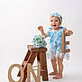 Ainhoa is registered to the contest to win money with this photo: baby, toddler, child, blue_dress, headband, flower_headband, wooden_step_stool, cardboard_letters, letter_e, letter_o, letter_n, hydrangea, bouquet, barefoot, white_background, studio, smiling, standing, props, birthday