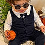 toddler, child, sunglasses, pumpkin, black_vest, bow_tie, curly_hair, white_shirt, sitting, indoor, plant, decor, striped_socks, cute, fashion, smile, hands, face, rocking, casual