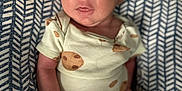 Enzo is registered to the contest to win money with this photo: baby, infant, newborn, onesie, patterned_clothing, cushion, fabric, indoor, portrait, cute, child, person, sitting, small, skin, face, hand, footwear, socks, relaxed