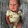 baby, infant, newborn, onesie, patterned_clothing, cushion, fabric, indoor, portrait, cute, child, person, sitting, small, skin, face, hand, footwear, socks, relaxed