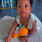 Mouminatou participe au concours pour gagner de l'argent avec cette photo : baby, child, crawling, plush_toy, carpet, indoor, person, curly_hair, bracelet, necklace, striped_clothing, flooring, furniture, wheel, home, cute, young_child, skin, hand, face