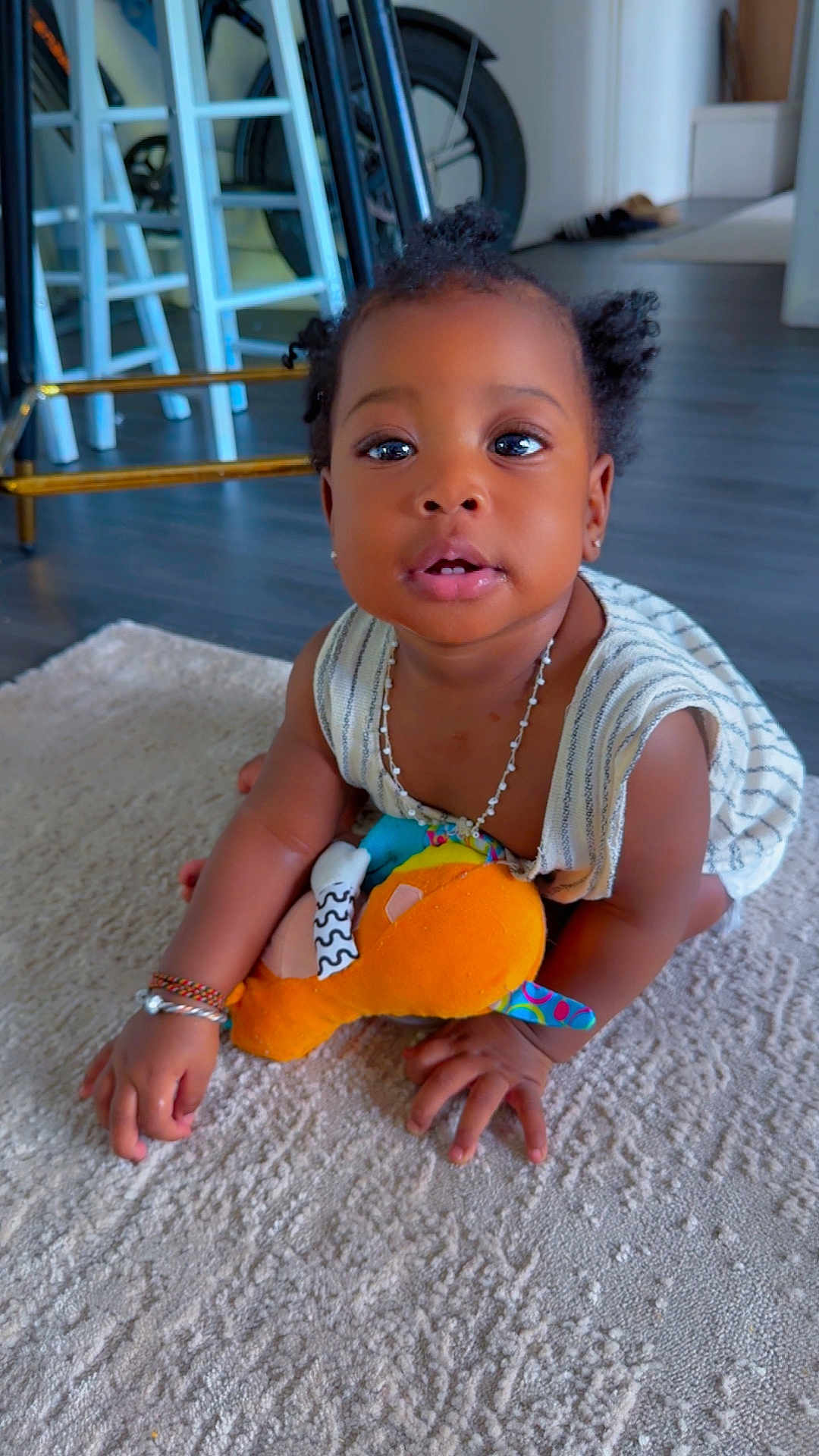 Mouminatou participe au concours pour gagner de l'argent avec cette photo : baby, child, crawling, plush_toy, carpet, indoor, person, curly_hair, bracelet, necklace, striped_clothing, flooring, furniture, wheel, home, cute, young_child, skin, hand, face