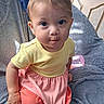 Jewlz joined the competition — help win amazing prizes! baby, child, infant, portrait, sitting, indoors, smiling, curious, face, eyes, brown_hair, yellow_shirt, pink_clothing, dress, blanket, bottle, bed, door, closeup, cozy