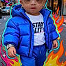 child, toddler, street, city, urban, puffer_jacket, blue_clothing, sunglasses, fashion, portrait, standing, serious_expression, storefronts, buildings, road, phone_screenshot, lock_screen, flame_graphics, colorful, outdoor
