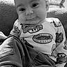 baby, child, infant, smiling, portrait, black_and_white, sitting, indoors, living_room, couch, clothing, shirt, cartoon, cars, race_cars, toy_theme, face, eyes, cozy, photography
