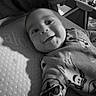 baby, infant, child, smiling, portrait, black_and_white, indoors, lying_down, mattress, sleepwear, patterned_clothing, face, eyes, mouth, happy, nursery, baby_gear, furniture, close_up, photography