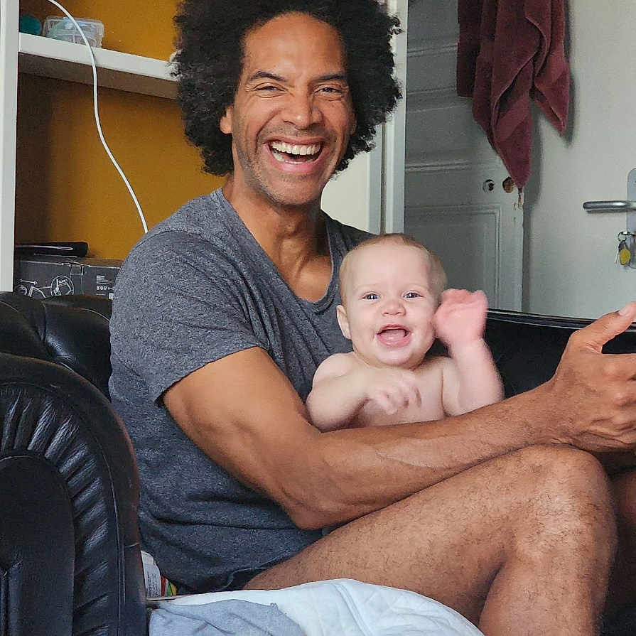 Shaddai a rejoint le concours — aidez-le/la à gagner de superbes lots ! adult, afro, arm, baby, blanket, casual, child, couch, family, furniture, happy, indoor, joy, living_room, person, sitting, skin, smiling, toddler, waving