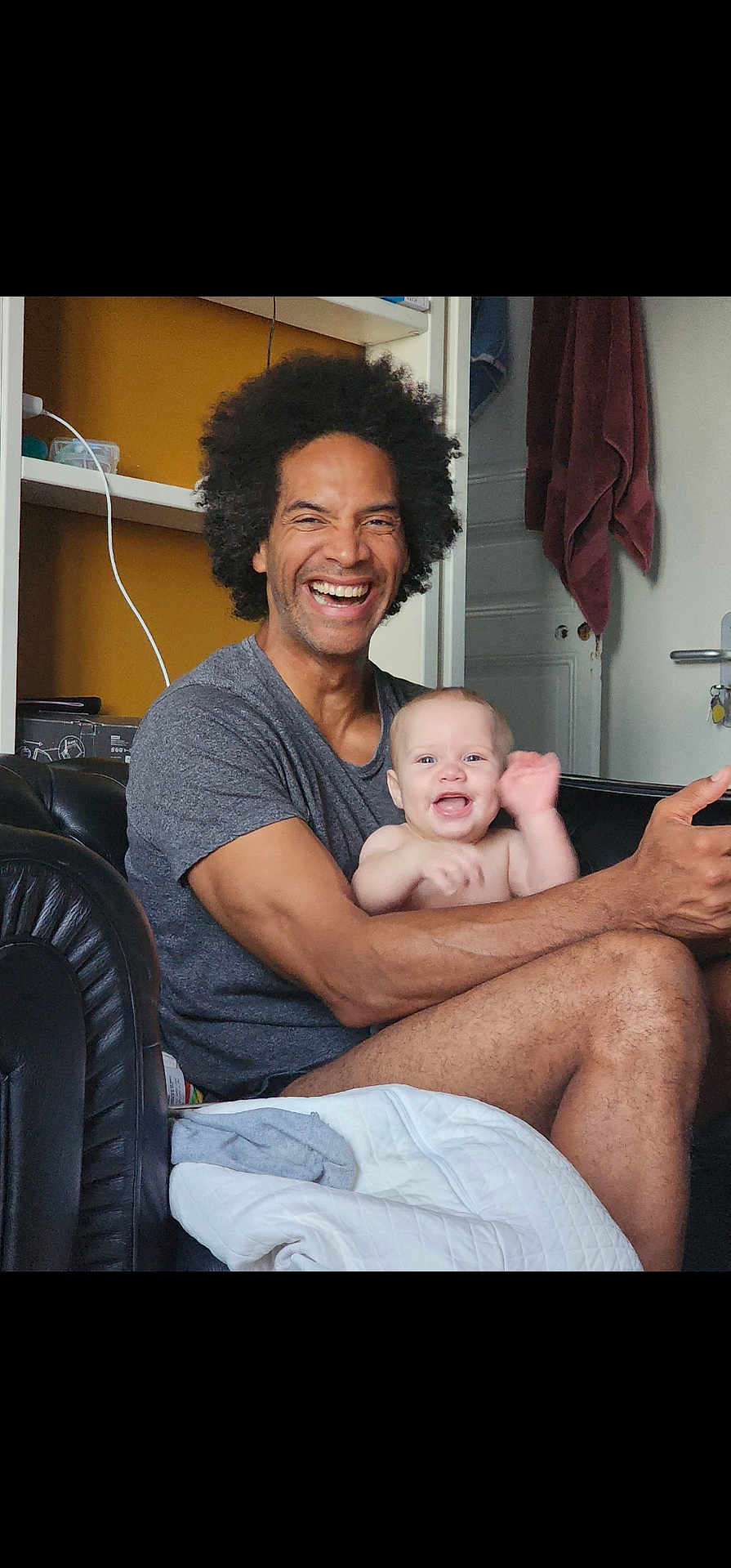 Shaddai a rejoint le concours — aidez-le/la à gagner de superbes lots ! adult, baby, smiling, happy, indoor, couch, afro, person, child, family, casual, living_room, blanket, furniture, arm, skin, waving, sitting, joy, toddler